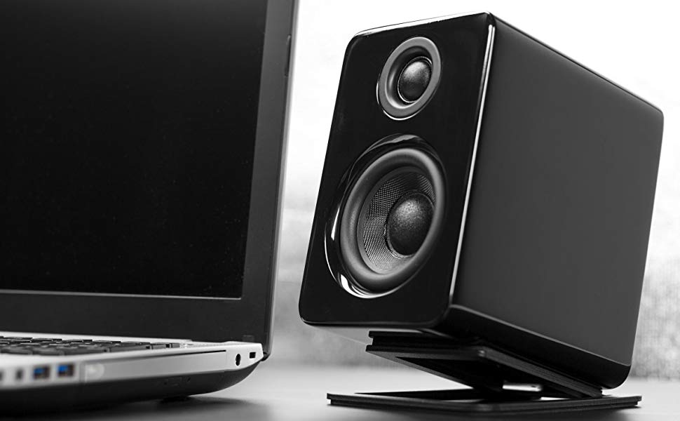 Kanto YU2 gloss black powered desktop speakers on desktop stands next to laptop